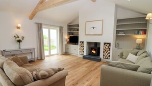 A spacious living room with a fireplace, wooden flooring, and built-in shelving. - Cotswold View (Witney)