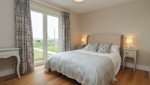 A bedroom with a large bed, two bedside tables with lamps, a view through a sliding glass door, and a ceiling light fixture. - Cotswold View (Witney)