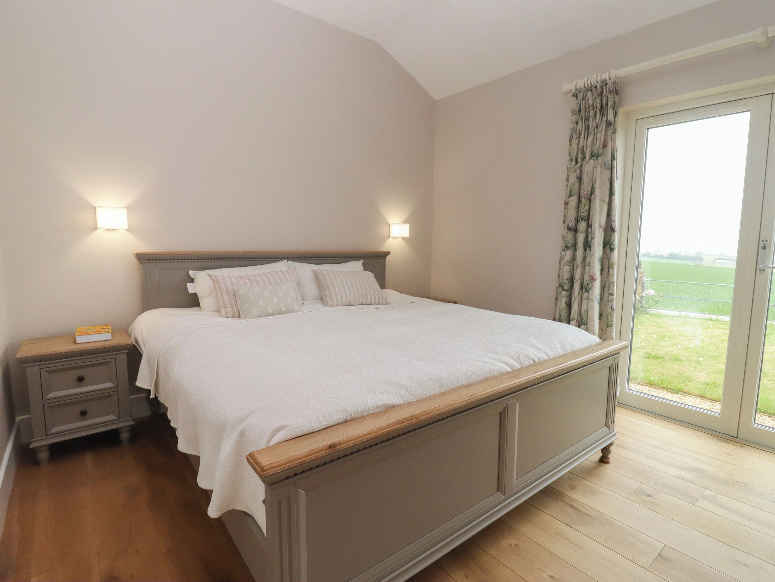 Ein Schlafzimmer mit einem großen Bett, zwei Nachttischen, einem Schreibtisch und Blick durch ein Fenster mit Vorhängen.