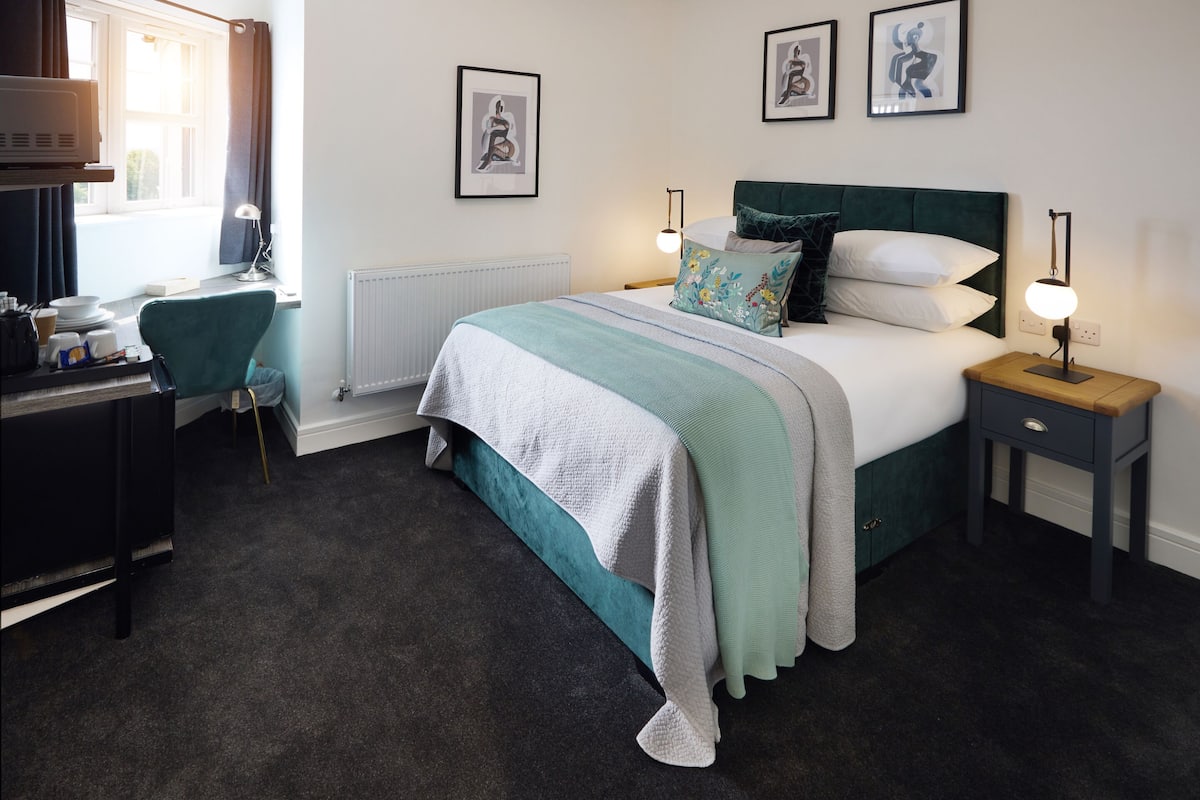 A neatly arranged bedroom with a bed, bedside tables, a desk, and a chair.