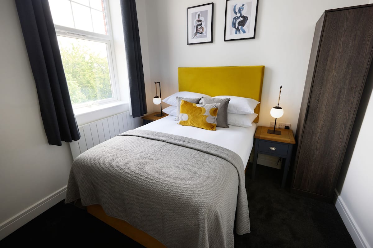 A neatly arranged bedroom with a bed, bedside tables, a wardrobe, and artwork on the wall.