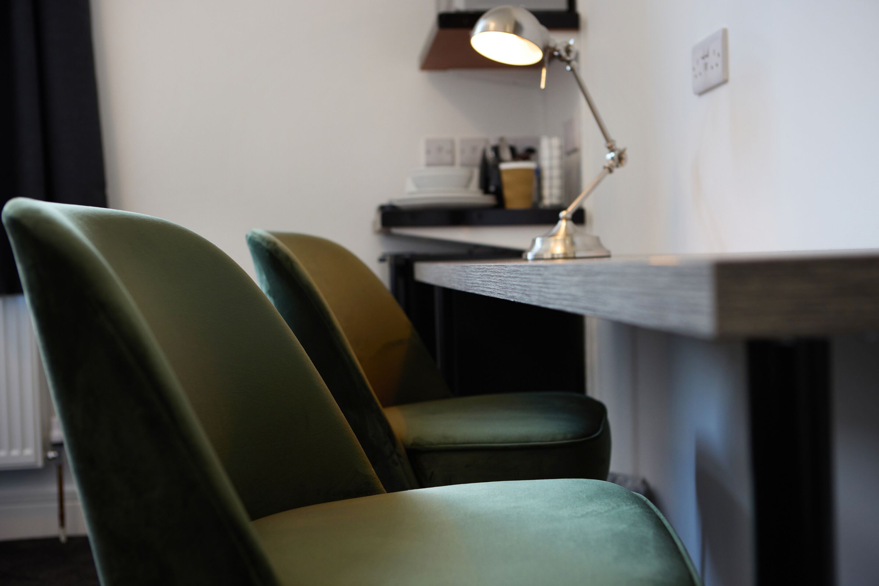 Ein Zimmer mit einem grünen Polsterstuhl und einem Schreibtisch mit Lampe.