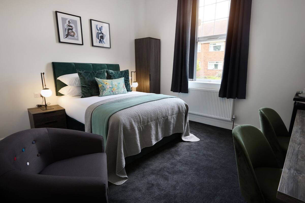 A bedroom with a bed, two bedside tables, a chair, a cabinet, and a window with curtains.
