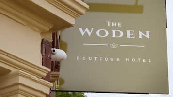 Señal del Hotel Woden Boutique, con un estilo arquitectónico clásico y una imponente torre del reloj al fondo.