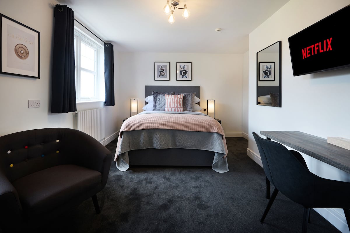 A bedroom with a bed, bedside lamps, a desk, a chair, a TV, and artwork on the walls.
