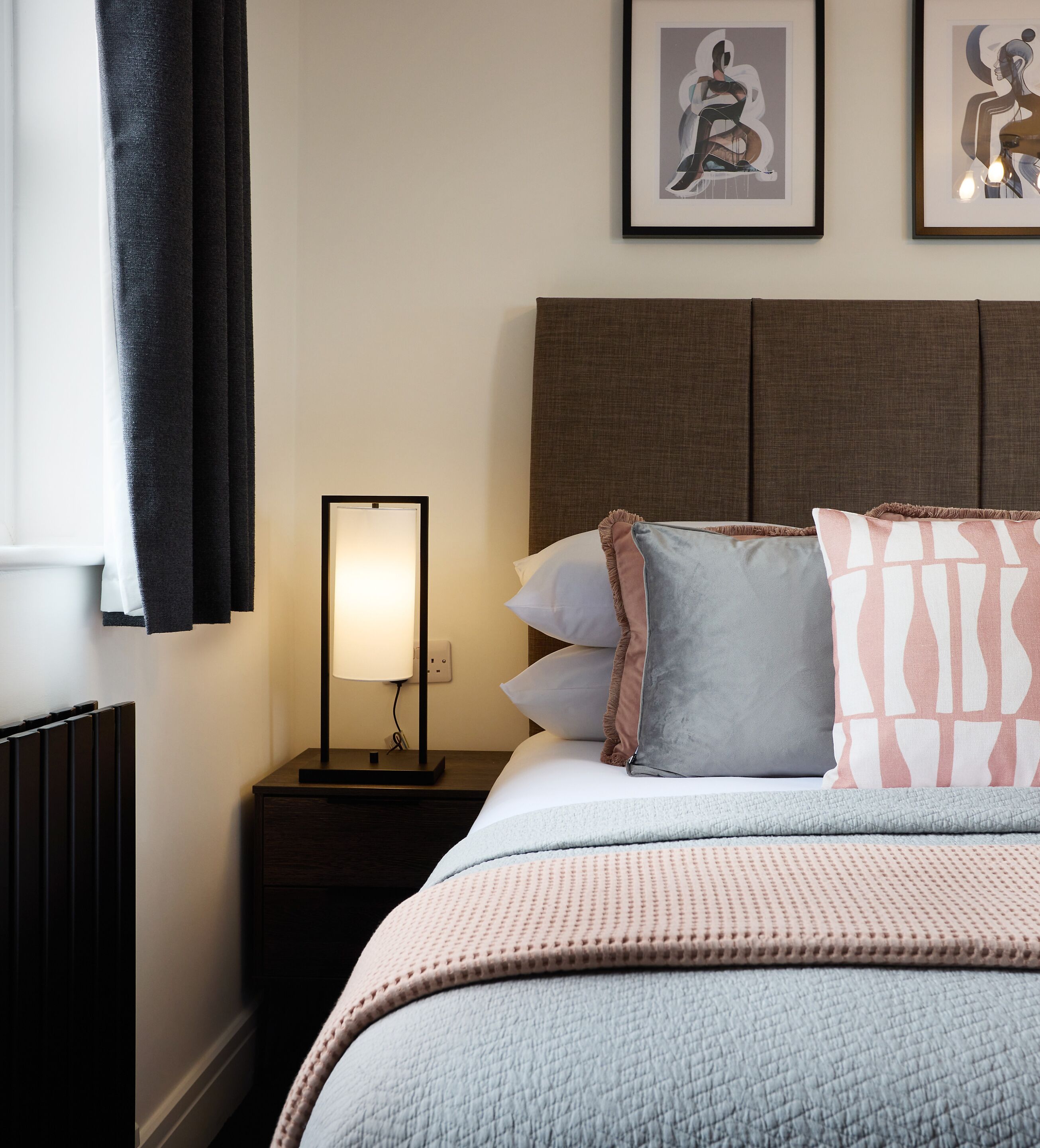 A neatly made bed with pillows and a blanket, a bedside table with a lamp, and a framed artwork on the wall.