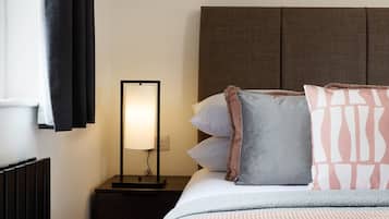 A neatly made bed with pillows and a blanket, a bedside table with a lamp, and a framed artwork on the wall.