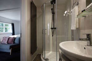Ein modernes Badezimmer mit einer gläsernen Duschkabine, einem weißen Waschbecken und einem Glastablett mit Toilettenartikeln.