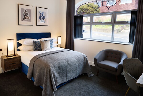 A bedroom with a bed, bedside tables, a chair, a desk, and a window with a view of the outside.