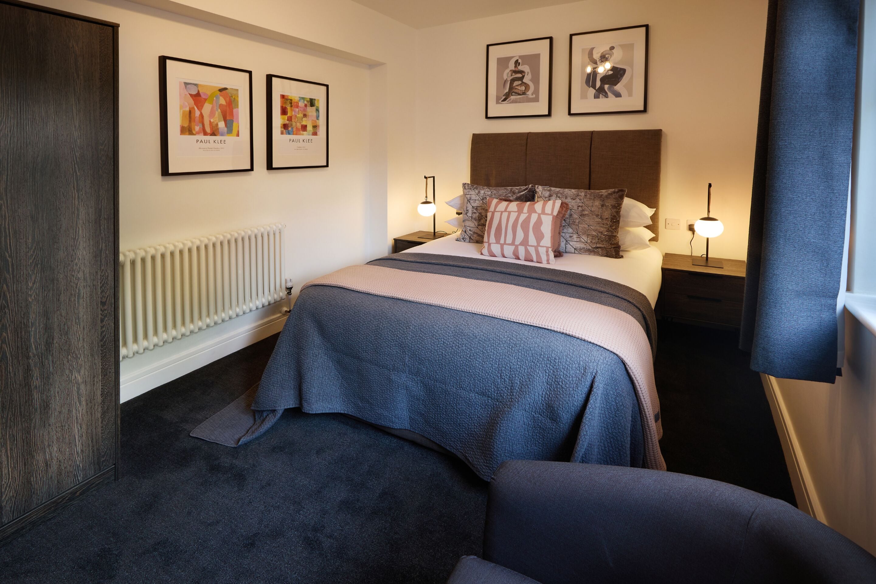 A modern bedroom with a large bed, a headboard, two bedside tables with lamps, and artwork on the walls.