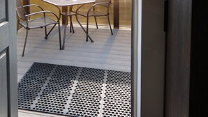 An open door to an outdoor patio with a table and chairs, a doormat, and a wooden fence in the background. - The Woden Boutique Hotel Walsall M6 J9 (Wednesbury)