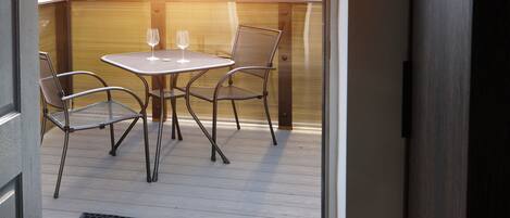 An open door to an outdoor patio with a table and chairs, a doormat, and a wooden fence in the background.