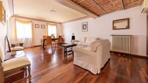 Un ampio soggiorno con soffitto alto, pavimento in legno, un divano bianco, un tavolo da pranzo con sedie e un camino.