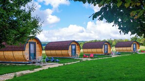 A row of wooden cabins with curved roofs, each featuring a door and windows, set in a grassy area with a clear sky.