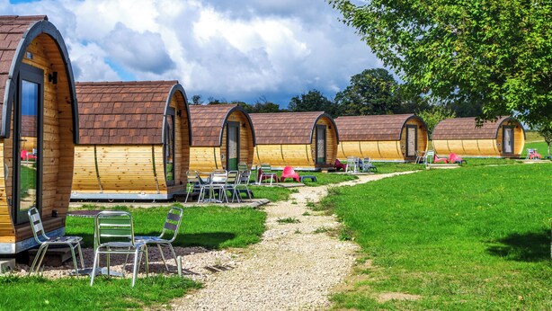 A row of wooden cabins with arched roofs, each with a door and window, and a gravel path leading to them.