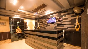 A modern reception area with a glass partition, a digital clock, and a television mounted on the wall. - Hotel Suncity  (Hisar)