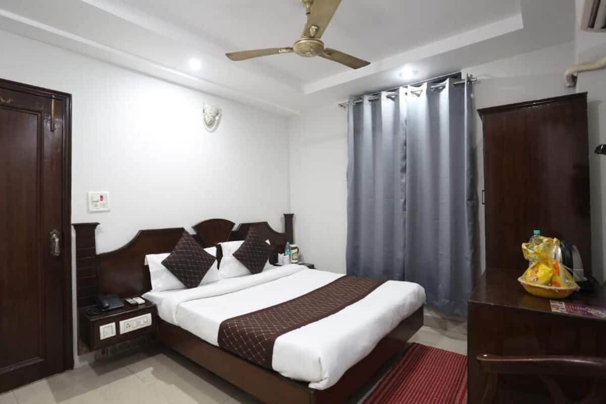 Ein Hotelzimmer mit Bett, Schreibtisch, Kleiderschrank, Deckenventilator und einem Fenster mit Vorhängen.