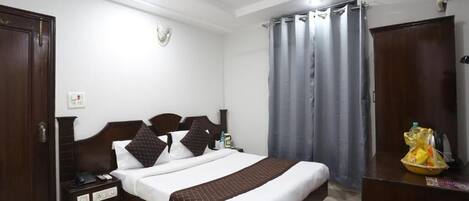 A hotel room with a bed, a desk, a wardrobe, a ceiling fan, and a window with curtains.