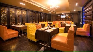A restaurant with orange and yellow seating, wooden paneling, and a chandelier. - Hotel Suncity  (Hisar)