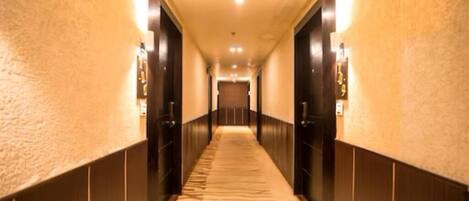A hotel hallway with a carpeted floor, wooden paneling on the walls, and a door at the end.