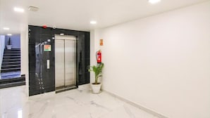 A modern hallway with a black elevator, a fire extinguisher, and a potted plant. - Hotel Suncity  (Hisar)