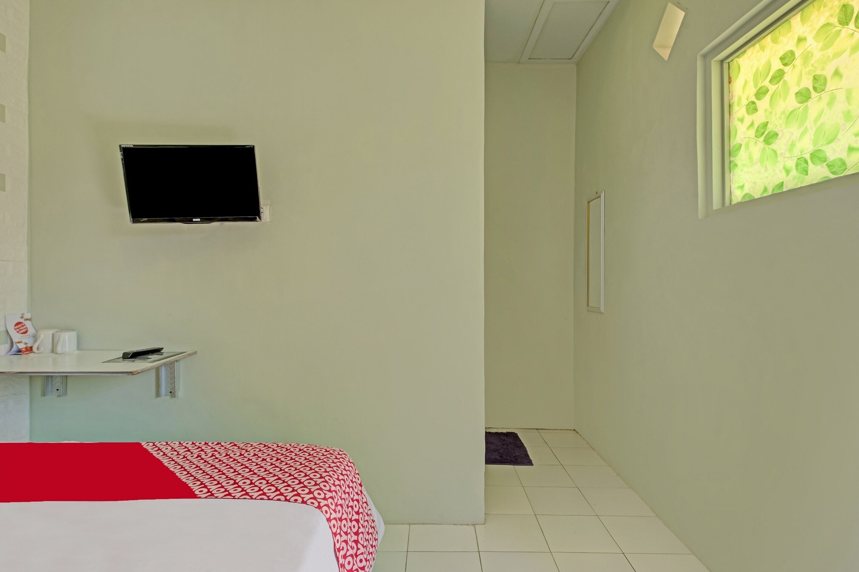 Quarto de hotel com uma cama, uma mesinha com chaleira, uma televisão e uma janela com padrão de folha.