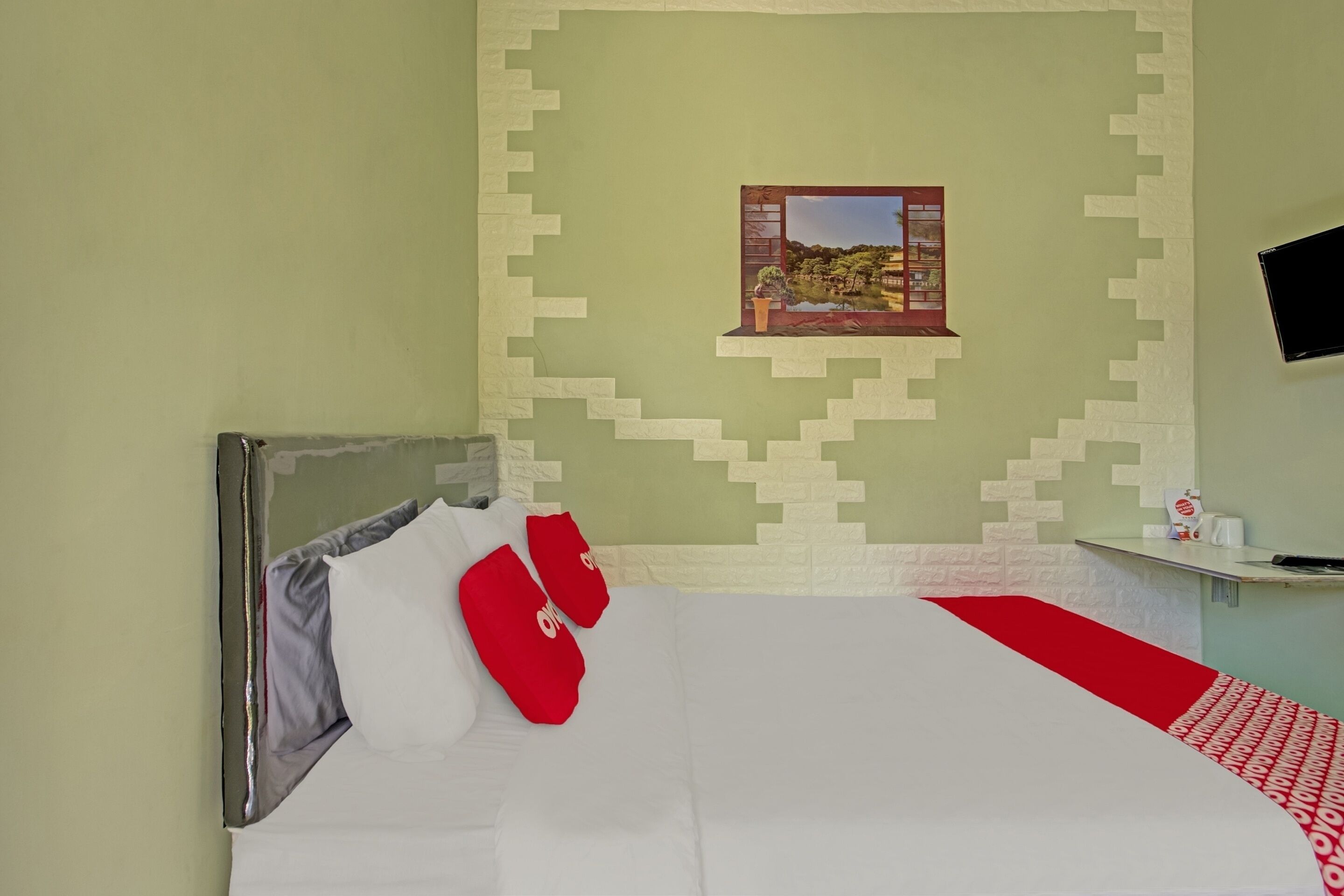 A hotel room with a bed, pillows, a small table, a wall-mounted TV, and a picture of a landscape.