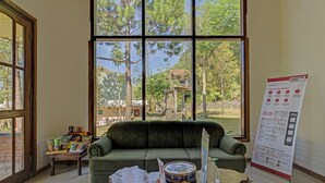 A room with a large window, a green sofa, a small table with snacks, and a poster on the wall. - Hotel O Villa Inn App Trawas Bintaro Syariah (Trawas)