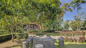 A garden with stone benches and a wooden table, surrounded by trees and a small building. - Hotel O Villa Inn App Trawas Bintaro Syariah (Trawas)