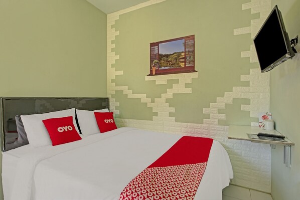 Une chambre d’hôtel avec un lit, des oreillers, une télévision, un tableau au mur et une petite table avec une tasse.