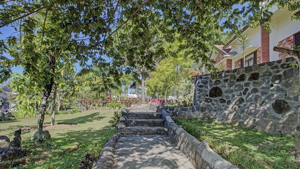 A stone pathway leading to a building with a stone wall and a flag. - Hotel O Villa Inn App Trawas Bintaro Syariah (Trawas)