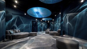 Eine moderne Lounge mit einer gebogenen Sitzecke, einem zentralen Tisch und einer großen, beleuchteten Deckeninstallation.