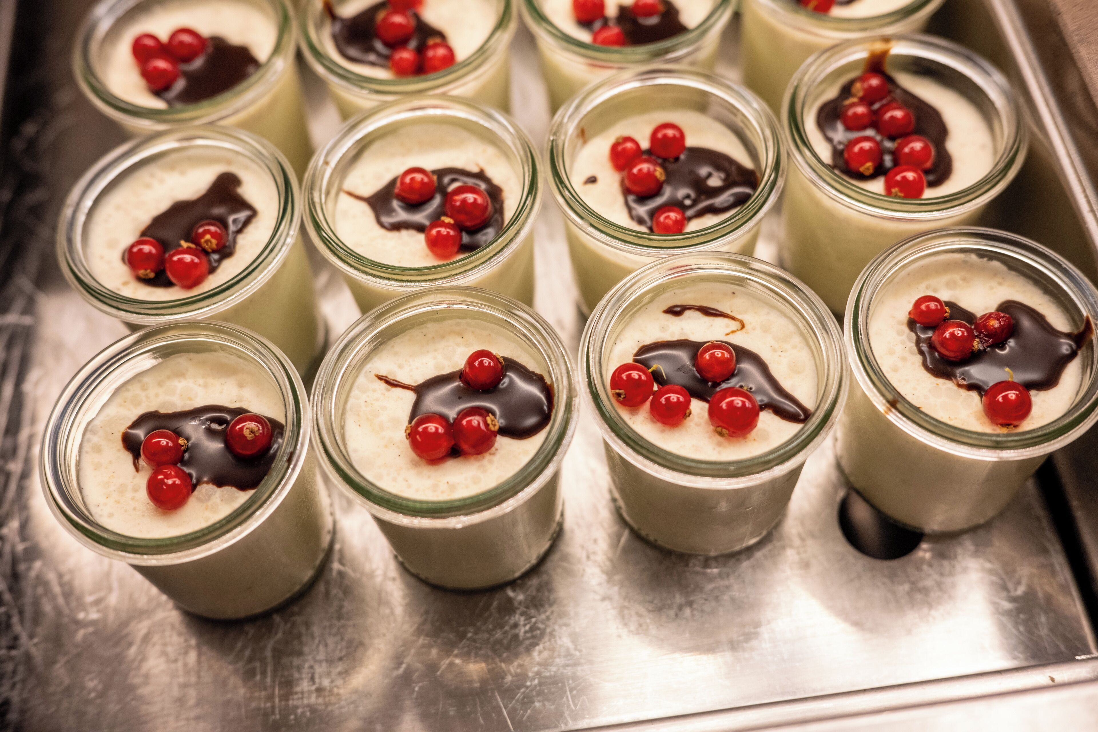A tray of dessert cups with a creamy filling, topped with red berries and chocolate drizzle.