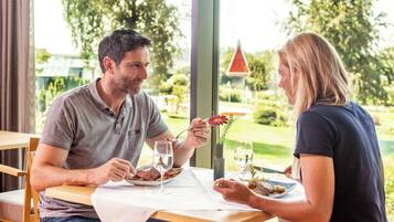 Une table à manger avec deux personnes assises, des assiettes remplies de nourriture et un vase avec des fleurs.