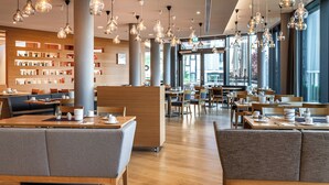 Ein modernes Restaurant mit mehreren Sitzbereichen, darunter Sitzecken und Tische, und einer großen Auswahl an Flaschen an der Wand.