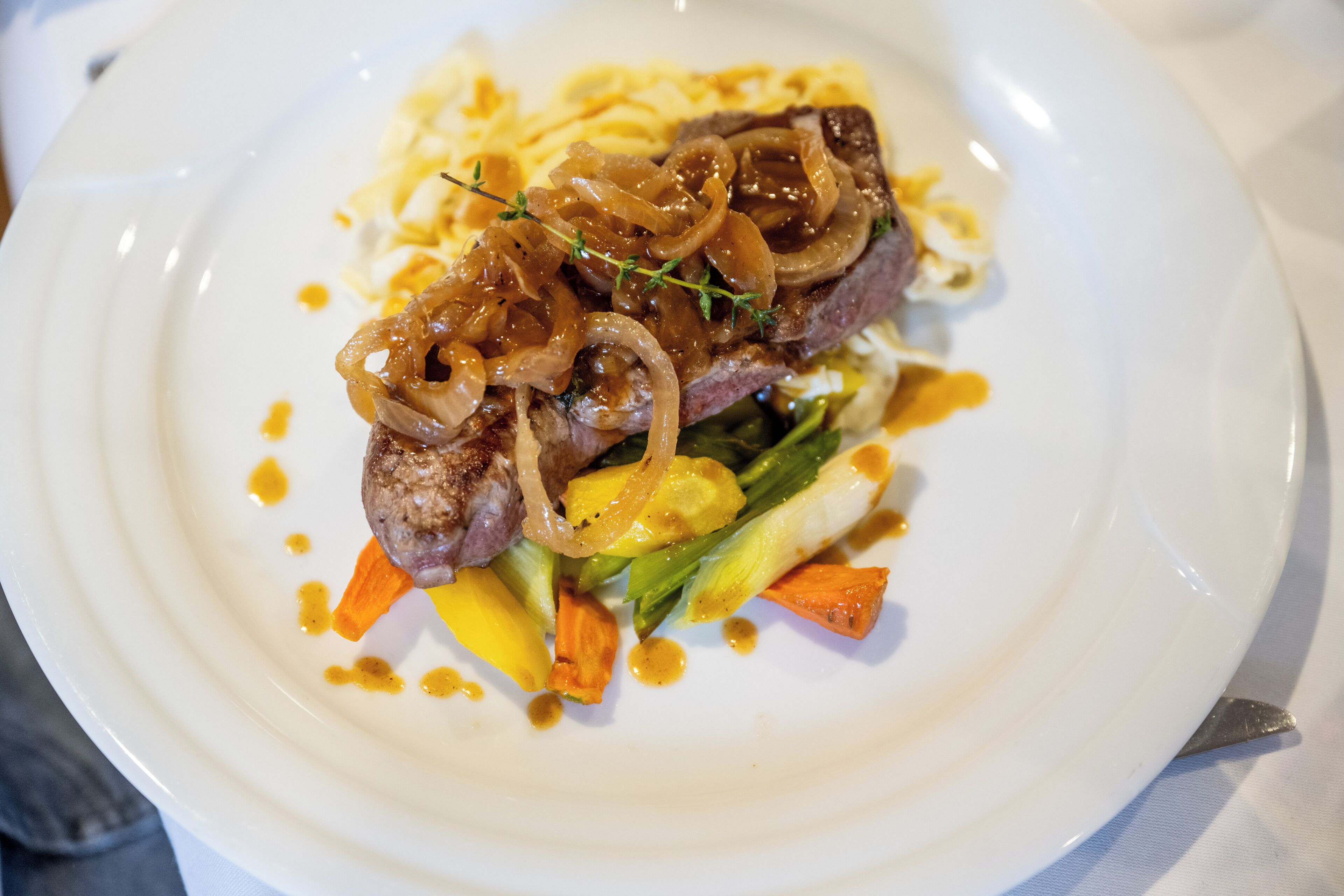 Un plato de comida con un bistec, verduras y cebollas caramelizadas.