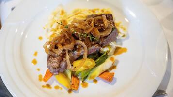 Un plato de comida con un bistec, verduras y cebollas caramelizadas.