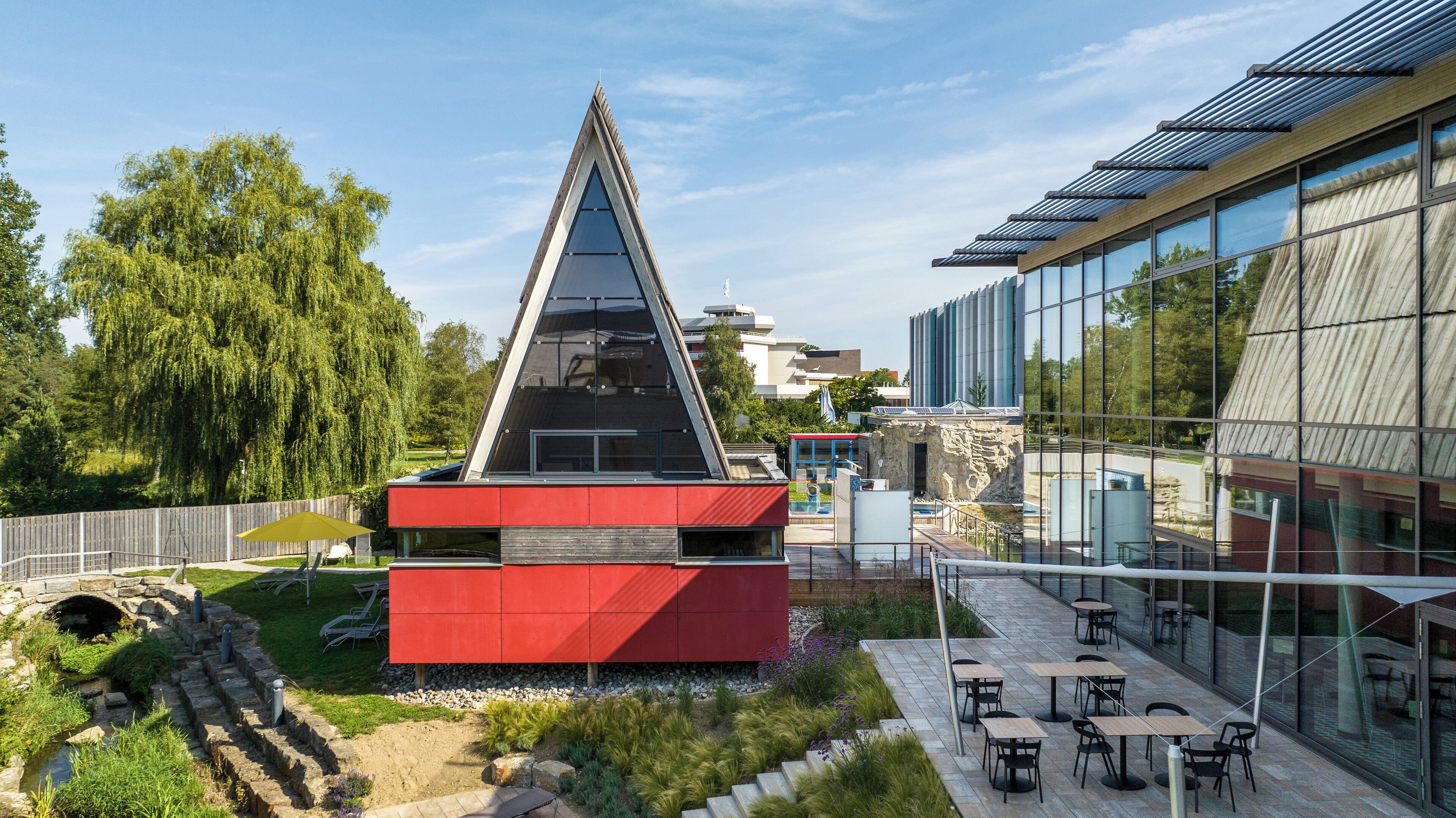 A modern building with a triangular roof, a red structure in front, and a glass facade.