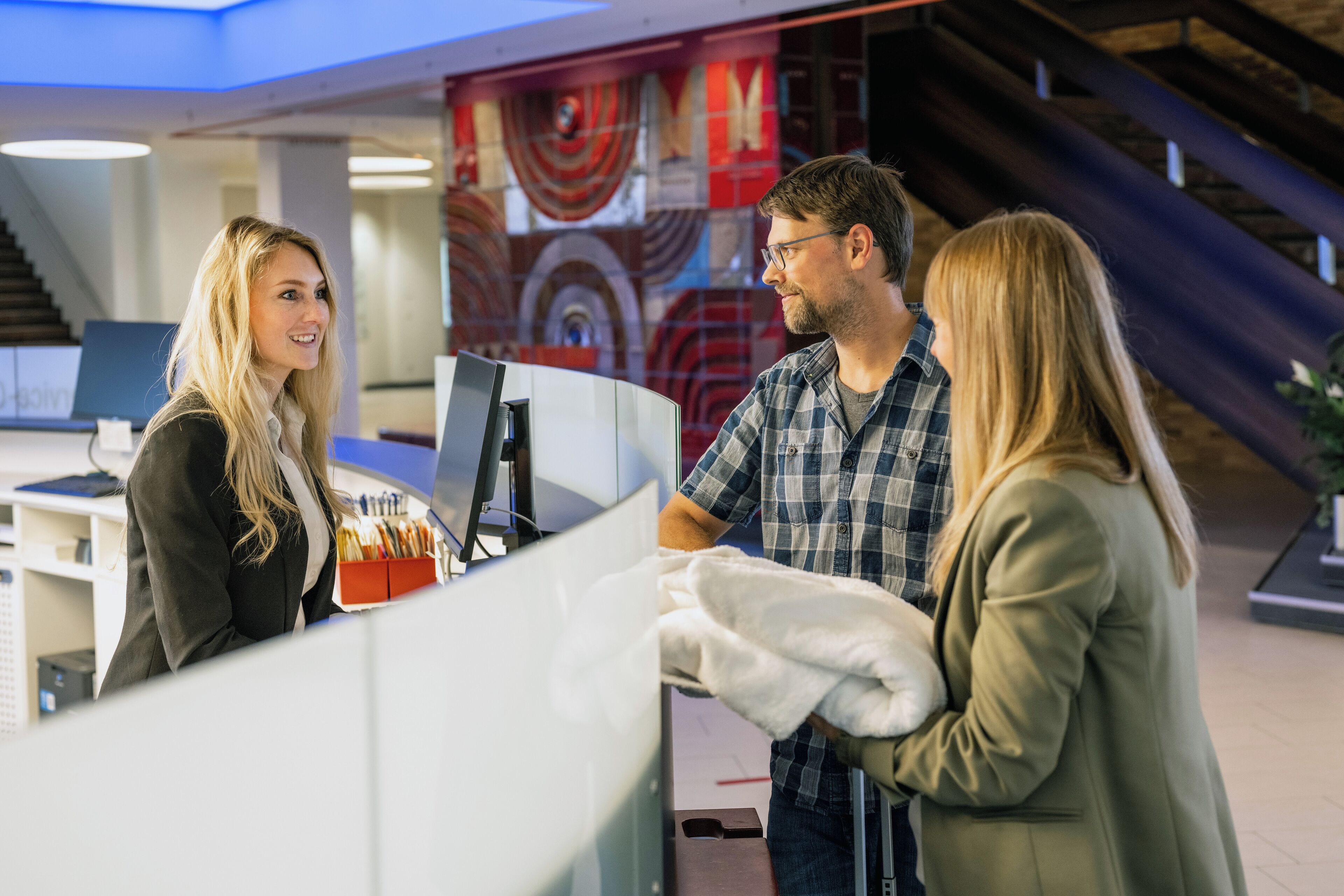 Een receptie met een balie, een computer en een trap op de achtergrond.