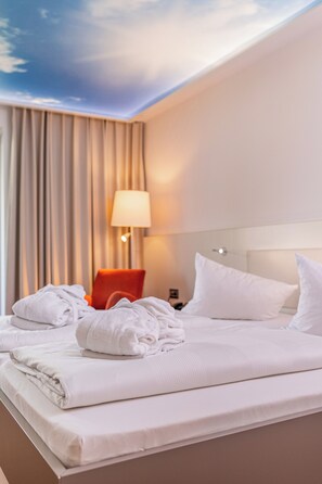 A hotel room with a neatly made bed, a red chair, a lamp, and a view of the sky through the ceiling. - Thermenhotel Gesundheits-Bad Buchau (Bad Buchau)