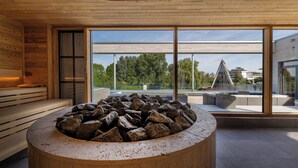 Ein modernes Interieur mit einem Steinkamin, Holzbanken und großen Fenstern mit Blick ins Freie.