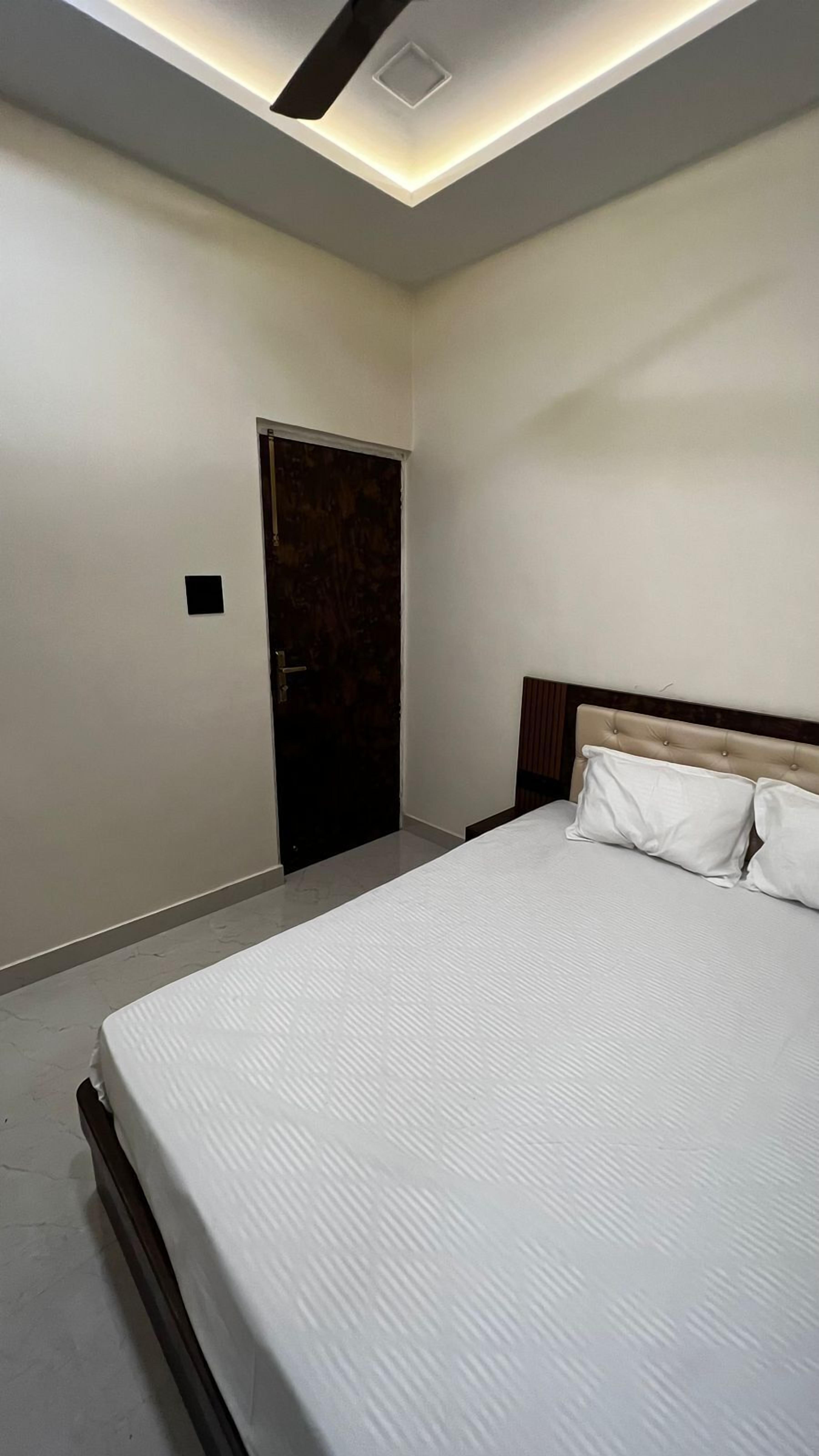 A bedroom with a large bed, a wooden headboard, a door, and a ceiling light fixture.