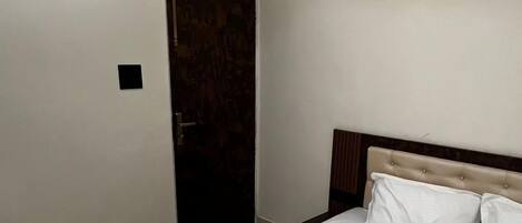 A bedroom with a large bed, a wooden headboard, a door, and a ceiling light fixture.