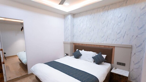 A modern hotel room with a large bed, a nightstand, a mirror, and a marble-patterned wall. - Hotel Divyakashi homestay (Varanasi)