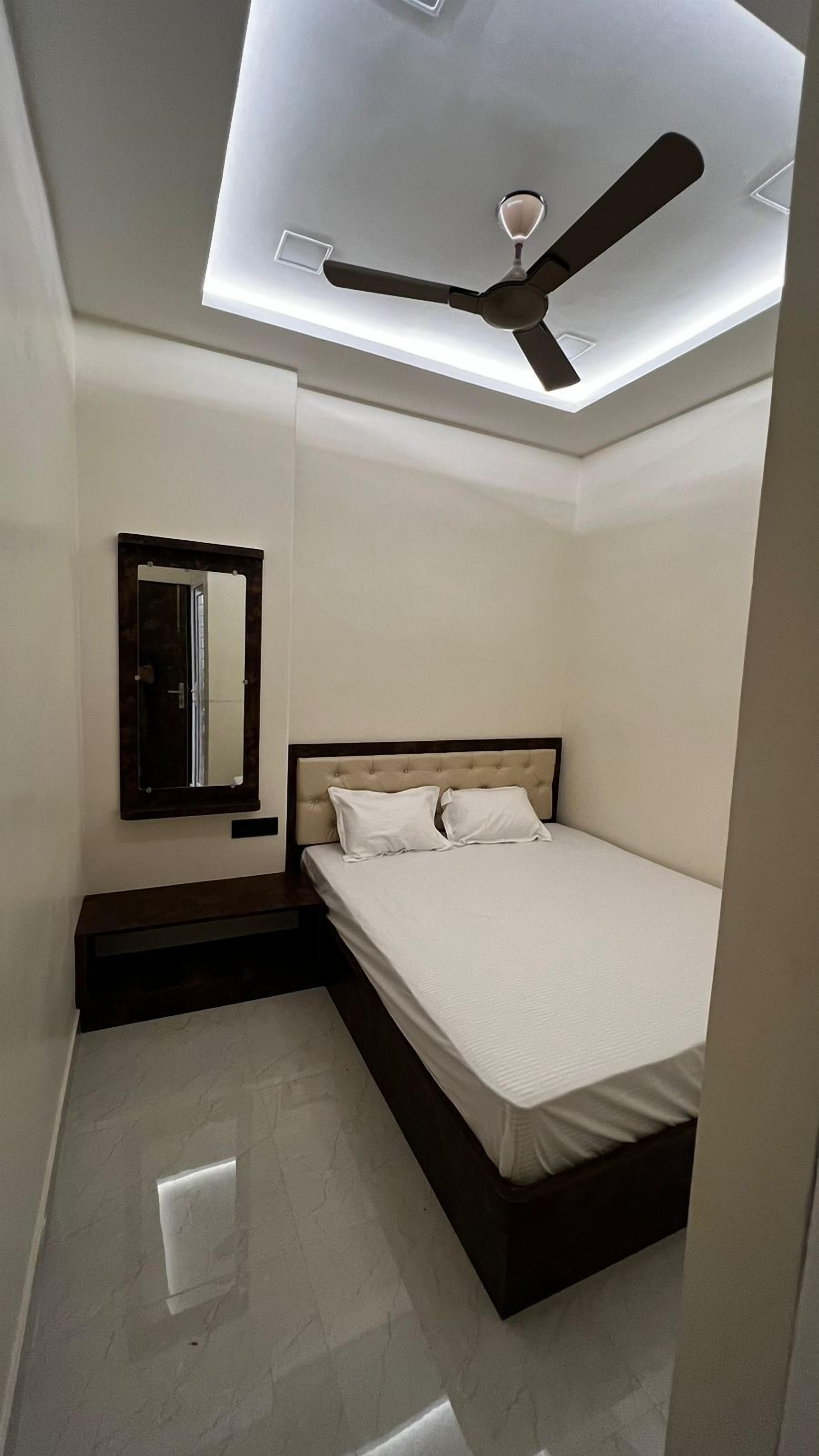 A bedroom with a bed, a ceiling fan, a mirror, and a light fixture.