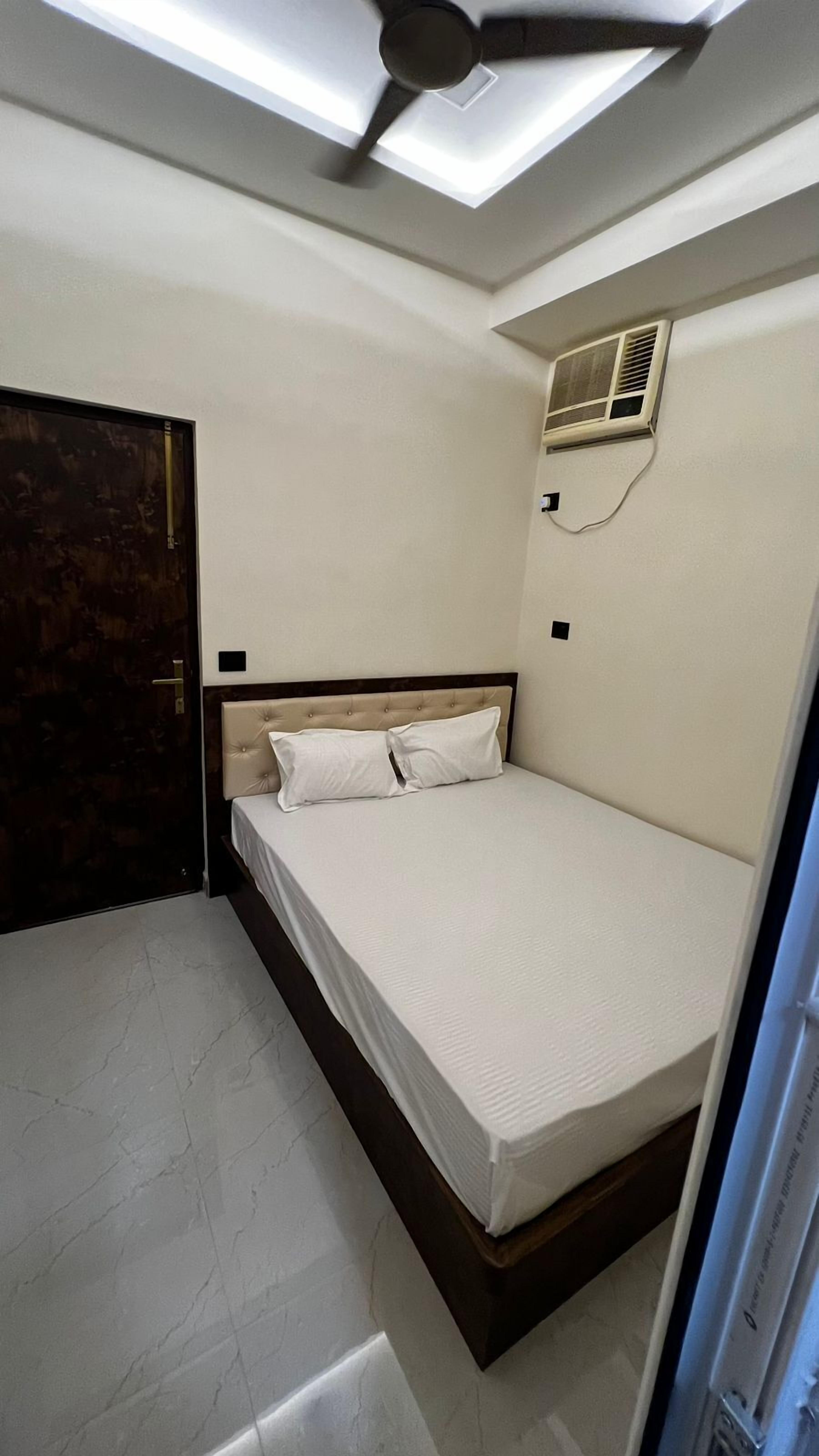 Une chambre à coucher avec un lit, un ventilateur de plafond, un appareil de climatisation et une porte.