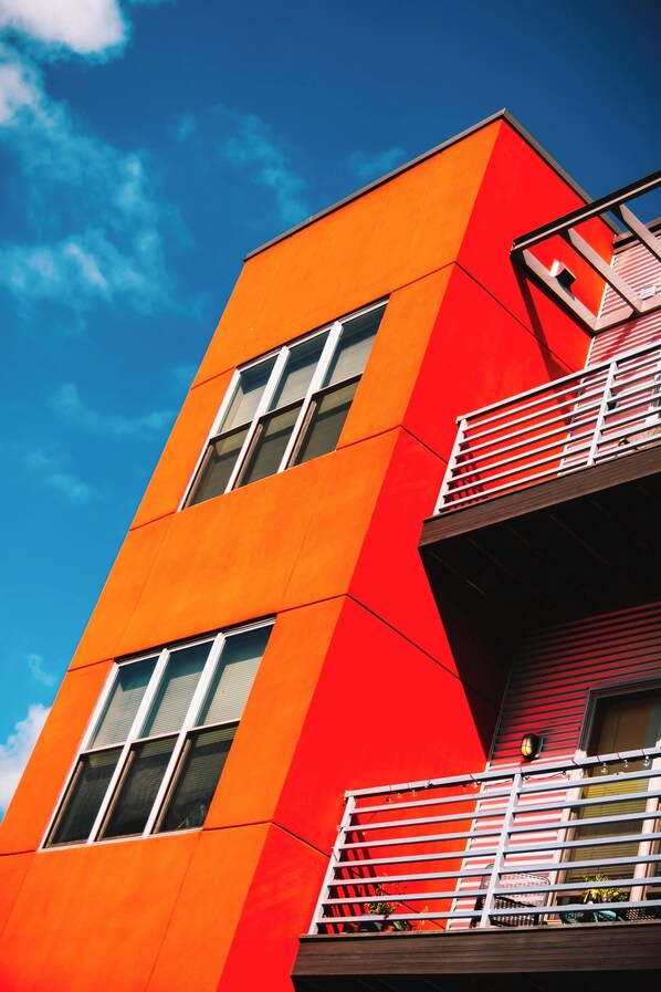 A modern building with a bright orange facade, large windows, and a balcony with a white railing.