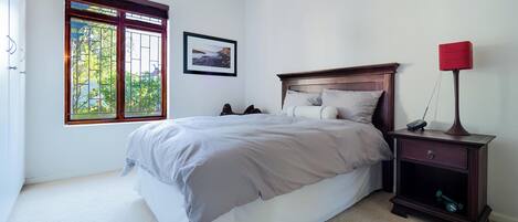 A bedroom with a bed, a nightstand, a lamp, a window with a view, and a framed picture on the wall.
