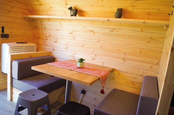 A compact room with a wooden wall, a small table with a tablecloth, a bench, and a heater.