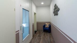Un pasillo con una puerta azul, un sillón azul con cojín estampado y un adorno colgado en la pared.